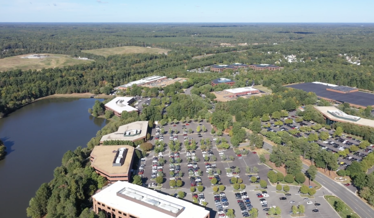Aerial view: office park, buildings, parking lots, lake, trees.